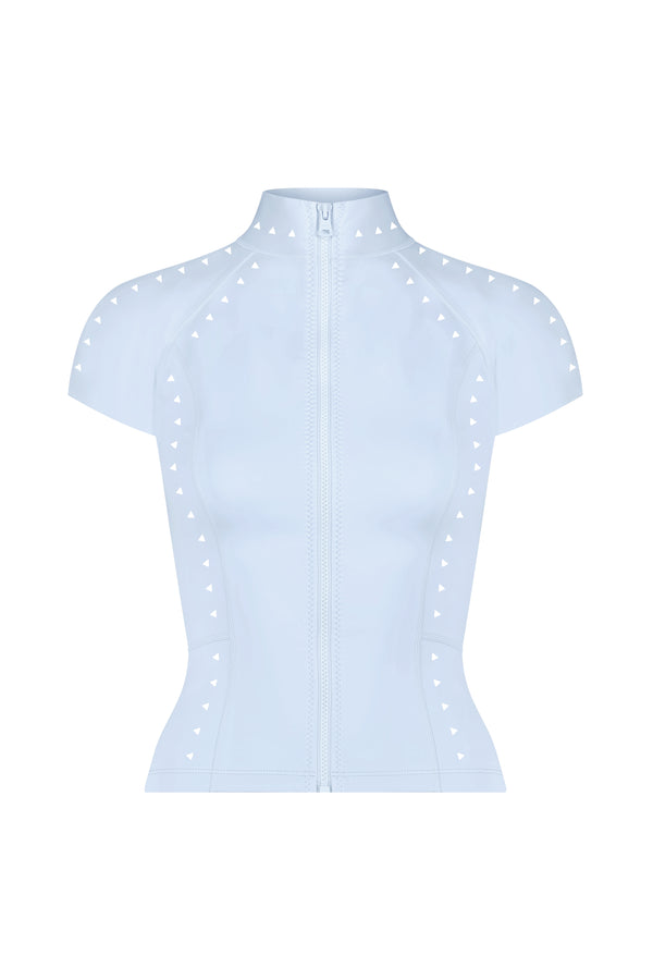 The Arden Top by Gigi C Bikinis is a light blue, short-sleeved, zip-up piece featuring a high collar and glossy scuba fabric. Its fitted design showcases decorative small white triangles on the seams and shoulders, enhanced by subtle laser-cut detailing.