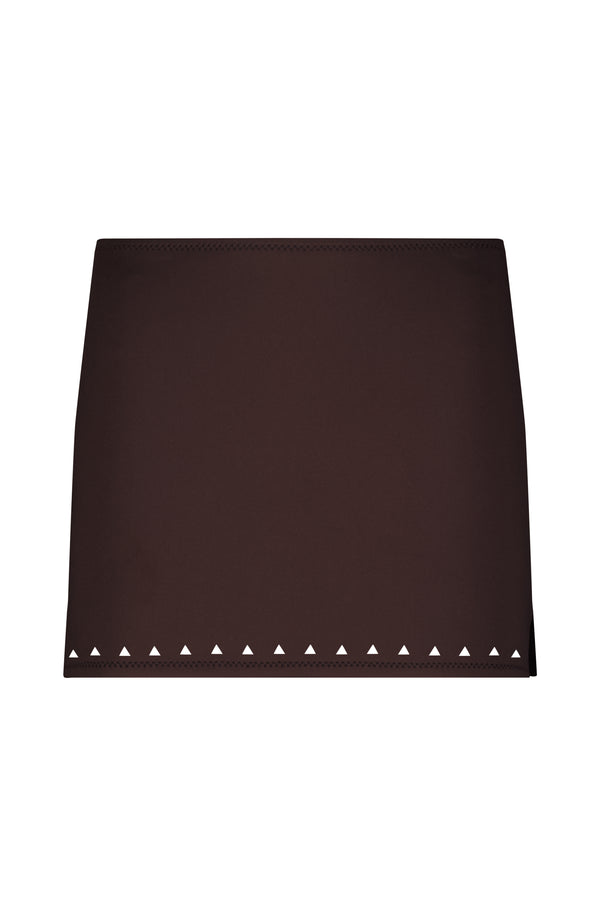 The Abby Skirt by Gigi C Bikinis from the Resort 2025 Collection is a brown mini skirt with a straight fit, featuring laser cutouts of small white triangles along the bottom hem.