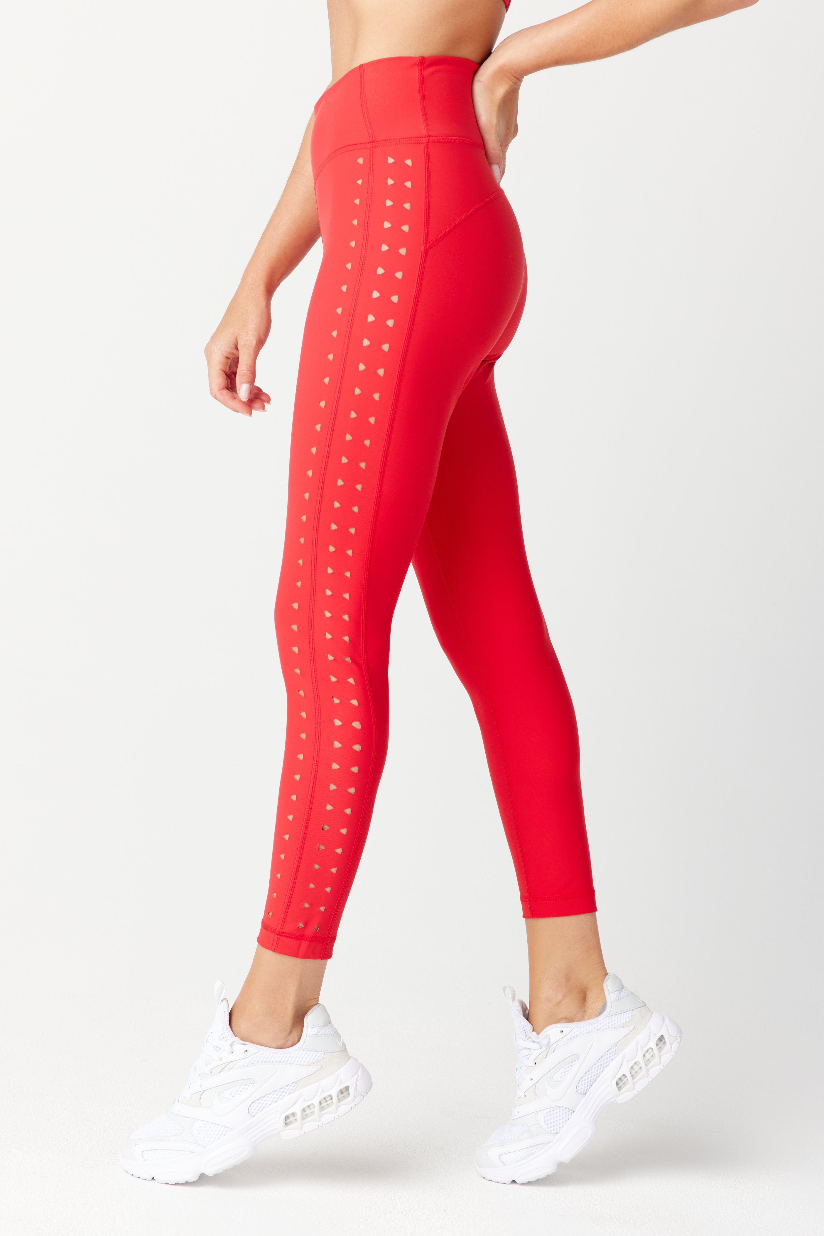 A person stands sideways against a light background, wearing Gigi C Sports Katrina Legging with high waist and laser cutouts down the sides, paired with white sneakers.