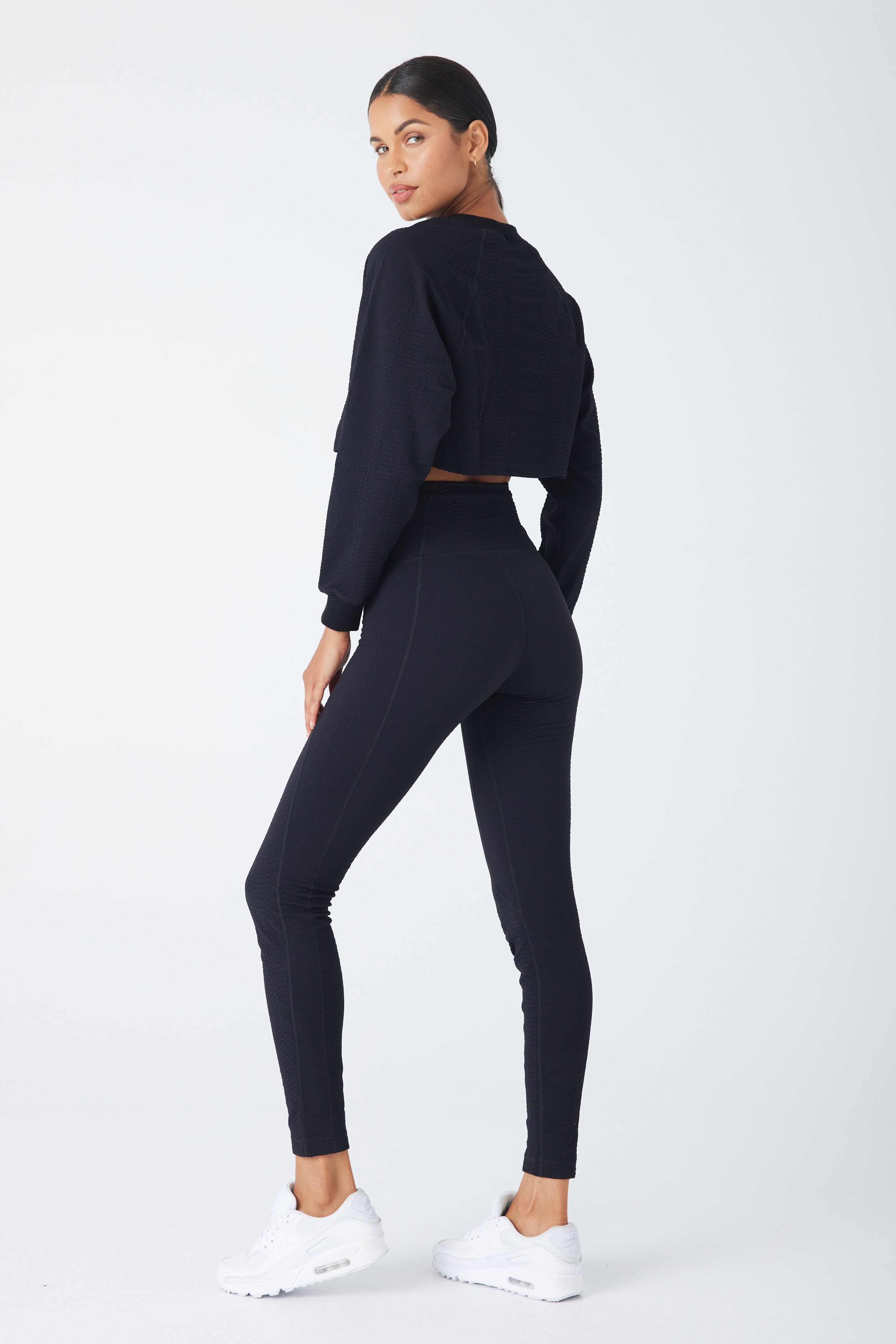 A person wearing the Isabella Pullover by Gigi C Sport and leggings with white sneakers poses against a plain background, angled slightly to the side with a confident expression.