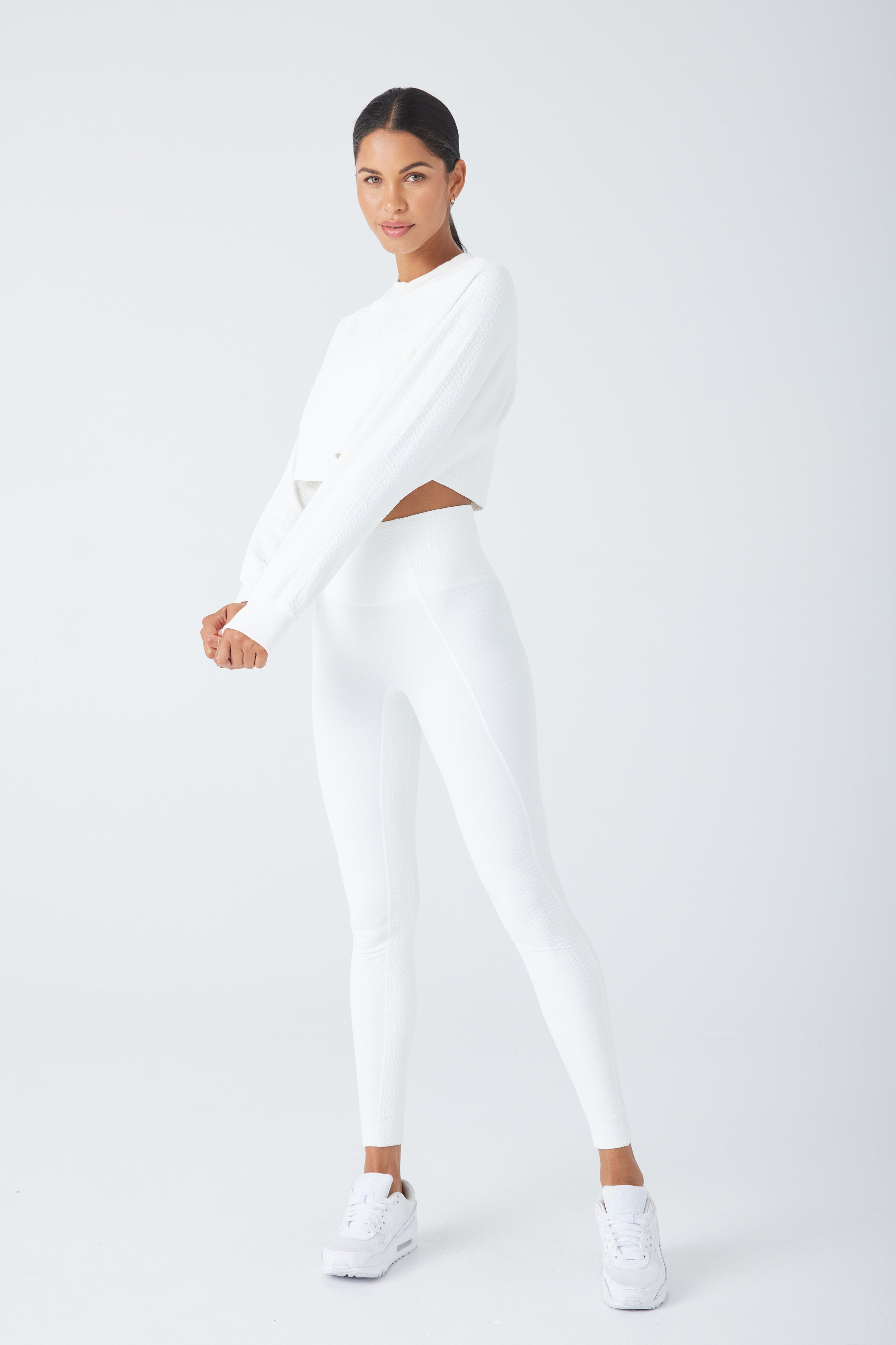 A person stands confidently in a relaxed pose, wearing an Isabella Pullover by Gigi C Sport with matching leggings and sleek sneakers. The plain light background enhances the elegance of the monochromatic outfit.