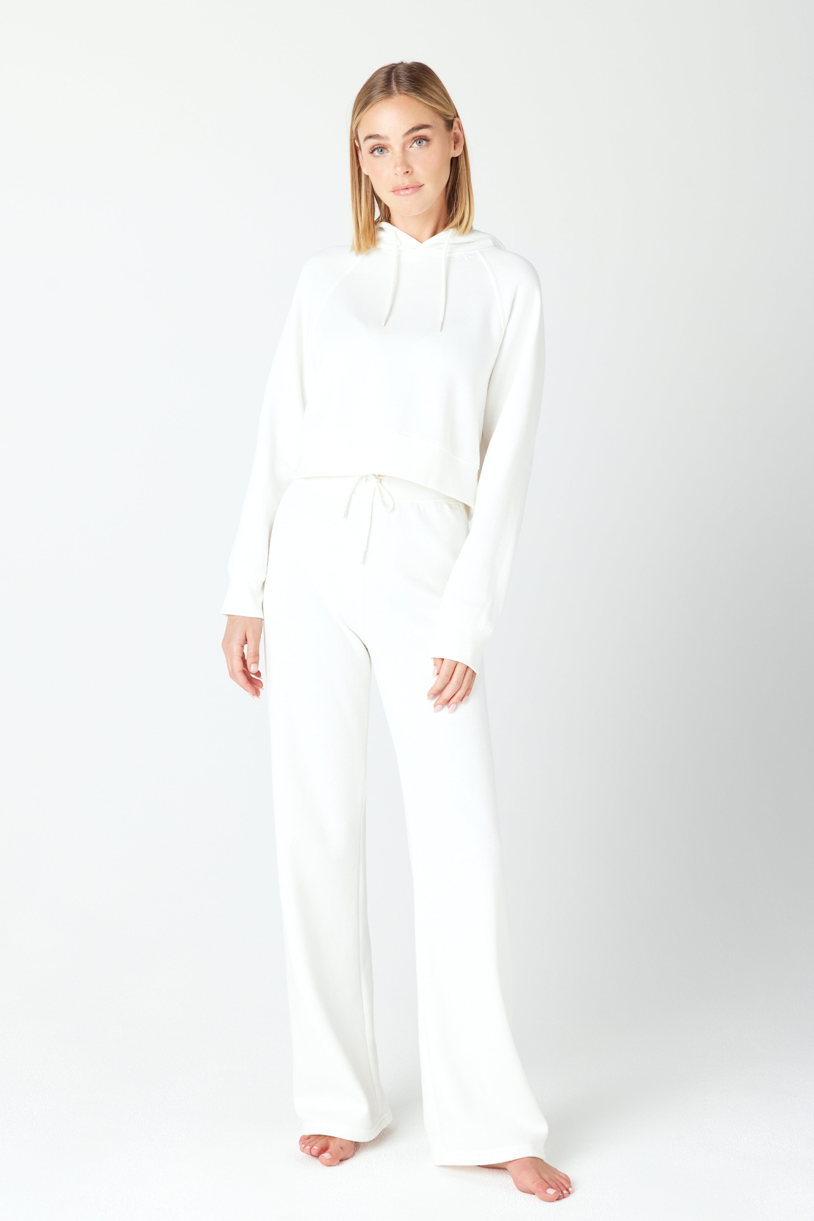 A person stands barefoot against a white backdrop, wearing a Gigi C Lounge Harlow Pant and Juliet hoodie, facing forward with a neutral expression.